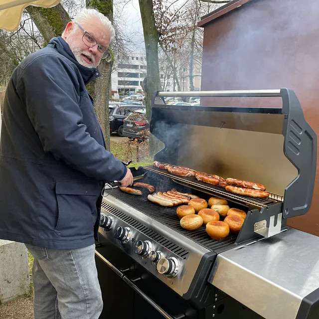 Auf einem großen Grill brutzeln Bratwürste und Brötchen