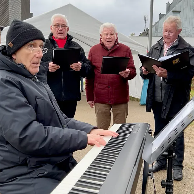 Der Chorleiter mit Mütze begleitet die Sänger am Keyboard