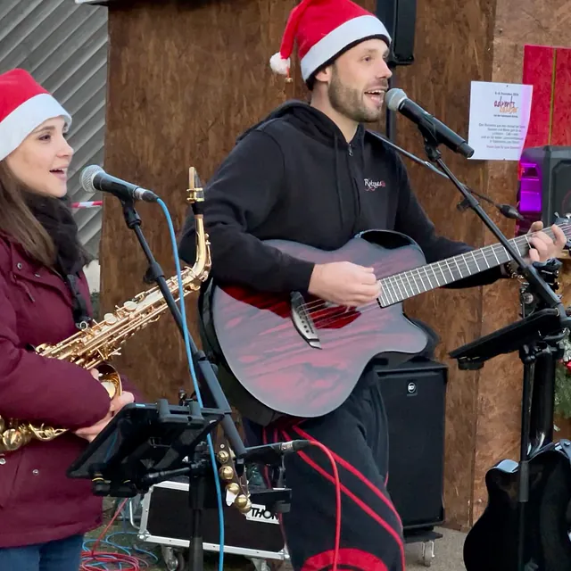 Die zwei Musiker, er mit Gitarre, sie mit Saxofon, singen ins Mikrofon